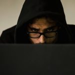 Serious young male programmer wearing black hoodie browsing netbook and hacking software in studio