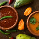 Top-down view of spicy Mexican salsas with peppers and fresh ingredients on a wooden table.