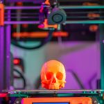 A vibrant 3D printed skull displayed on a printer in a colorful workshop setting.