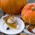 Slice of pumpkin pie with whipped cream, surrounded by pumpkins and autumn leaves, perfect for fall celebrations.