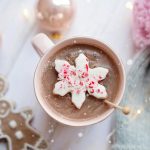 Delicious hot chocolate topped with a snowflake candy, surrounded by gingerbread cookies and baubles for a cozy winter feel.