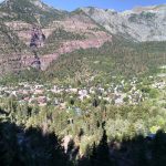 Beautiful aerial view of Ouray, Colorado surrounded by lush trees and majestic mountains under a clear sky.