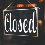 A close-up of a 'Closed' sign hanging against a blurred, bokeh background, creating a warm, inviting atmosphere.